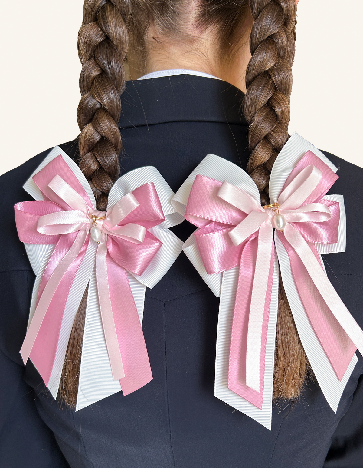 Pink Pearl horse show bows worn on two braids against a navy riding jacket